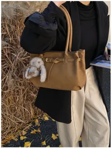 Vintage brown frosted tote bag with belt buckle and bunny charm, held by a model.