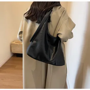 Close-up of a large black retro hobo tote bag carried on the shoulder over a beige coat
