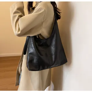 Close-up of a vintage black faux leather hobo shoulder bag worn by a model in a trench coat