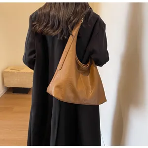 Close-up of a vintage brown leather tote bag worn by a model in a minimalist room.