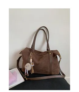 Large vintage brown suede Boston handbag with fuzzy monster charm against a white wall
