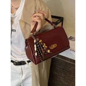 Detailed view of a vintage minimalist burgundy leather handbag with a decorative beaded tassel