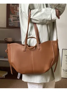 Large brown bucket tote bag with white contrast stitching carried by a model on shoulder