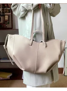 Large beige pleated tote bag carried by a model in a light green coat