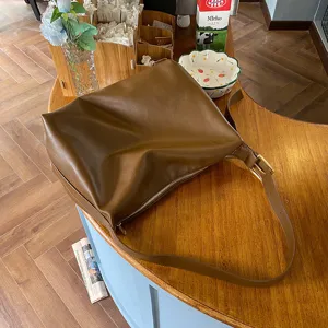 Detailed view of minimalist brown soft leather shoulder bag on a rustic wooden table