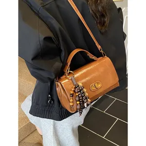 Detail of retro brown leather handbag with wooden bead charm being worn cross-body.