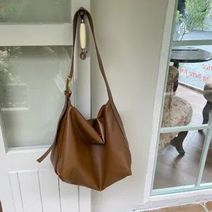 Minimalist brown soft leather shoulder bag hanging gracefully on a vintage door handle