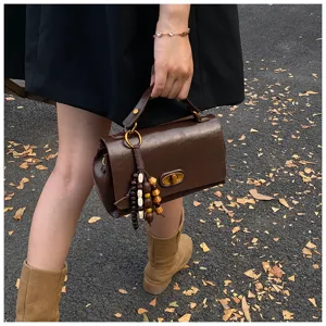 Vintage brown leather-like handheld bag with wooden bead tassel in outdoor lifestyle setting
