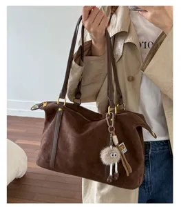Detail of large brown suede bowling bag with fluffy charm held by a model.