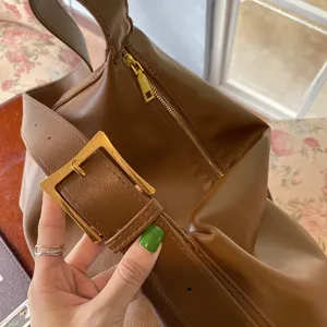 Close-up detail of a minimalist brown soft leather commute bag with a gold metal buckle