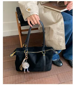 Close-up of a large black suede bowling bag with a cute monster charm held by a model