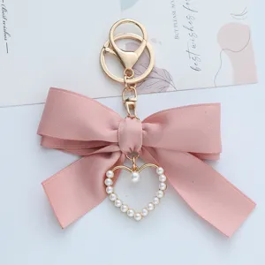 Close-up detail of pink silk ribbon bow keychain with pearl heart charm accessory.