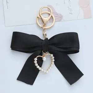 Close-up of black ribbon bow keychain with pearl heart pendant and gold clasp