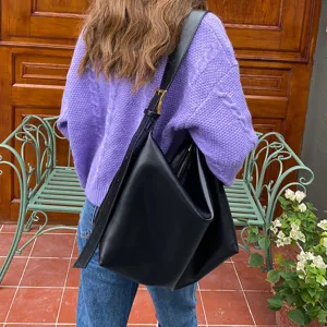 Detail view of a large black minimalist hobo bag worn over the shoulder in a lifestyle setting.