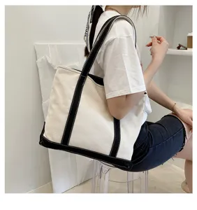 Model carrying a large off-white canvas tote bag with black contrast straps and base