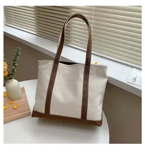 Classic canvas tote bag featuring brown trim and long shoulder straps on a white table