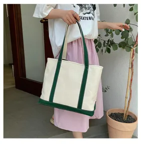 Large canvas tote bag with green trim held by a person in a casual outfit