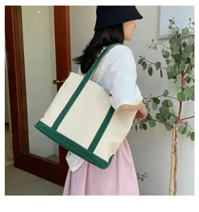 Detailed view of a large cream canvas tote bag with green handles on model's shoulder