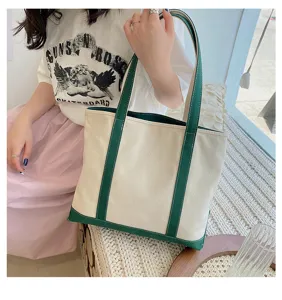 Close-up of a stylish off-white canvas tote bag with green trim held by a model