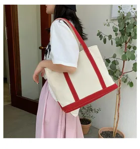 Detail view of a large capacity canvas tote bag with red handles carried by a female model