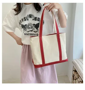 Macro view of large canvas tote bag with red handles and base worn by female model.