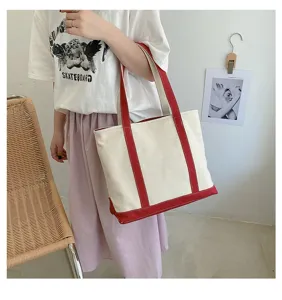 Lifestyle shot of a woman carrying a large canvas tote bag with red strap details.