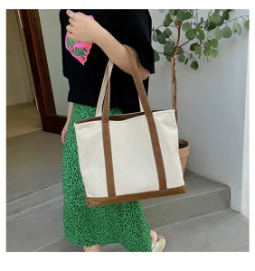 Large capacity canvas tote bag with brown handles carried by a model in casual outfit