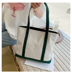 Lifestyle detail of a durable cream canvas tote bag with dark green handles and base.