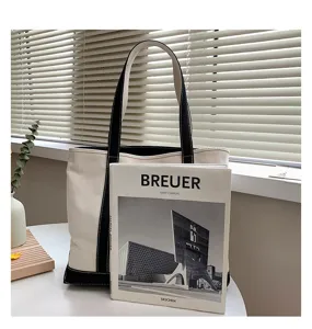 Large canvas tote bag with black contrast trim next to an art book for size reference
