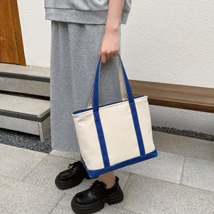Large capacity canvas tote bag with blue trim held by a model in casual grey outfit