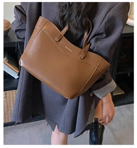 Detail view of a vintage brown soft leather tote bag worn by a model in a casual setting