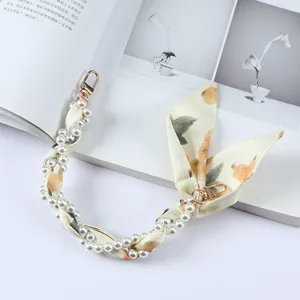 Detailweergave van een elegante polsband voor telefoon van parels en zijden sjaal met gouden sluiting