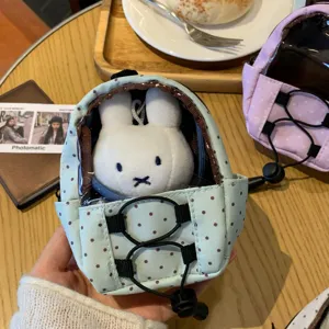 Detail view of a mini blue polka dot backpack doll pouch containing a white rabbit plush