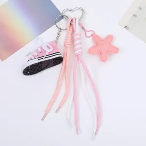 Detailed view of a pink miniature canvas sneaker and star charm keychain with braided ropes