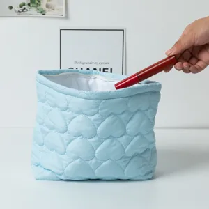 Detailed view of heart quilted makeup bag in light blue being filled with cosmetics