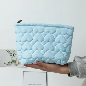 Detailed view of a light blue quilted heart pattern cosmetic pouch being held by hand.