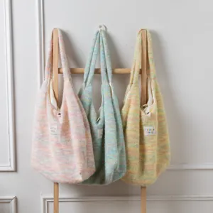 Drei bunte, gestrickte Plüsch-Einkaufstaschen in Regenbogen-Pastelltönen an einem Holzständer