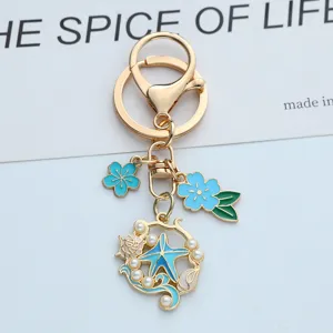 Détail d'un porte-clés thème océan avec étoile de mer et fleurs en émail bleu