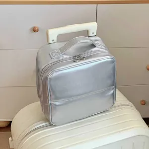 Metallic silver PU leather cosmetic storage bag shown on top of a white suitcase