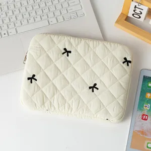 Detailed view of cream quilted laptop sleeve featuring cute black embroidered bows