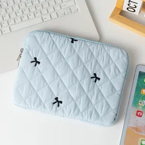 Light blue quilted laptop sleeve with black embroidered bow pattern on a white desk.