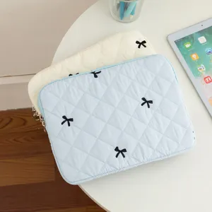 Quilted tablet sleeve with embroidered black bows shown on white workspace table