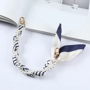 Detailweergave van de luxe telefoonriem van parels en gestreepte zijde met goudkleurige clips