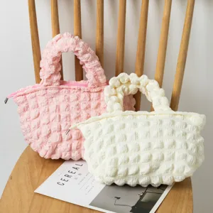 Juego de bolsos de mano con textura de burbujas plisadas rosa y crema en una silla.