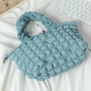 Detalle de un bolso de mano azul claro con textura de burbujas plisadas sobre fondo blanco