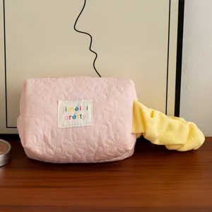 Pink quilted floral cosmetic bag with colorful embroidered patch and yellow scrunchie