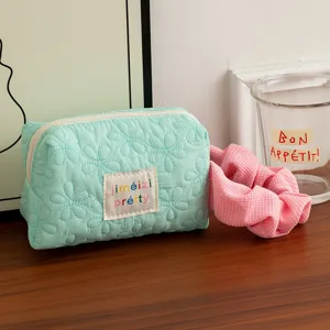 Detailed close-up of a mint green quilted cosmetic bag featuring floral stitching and label.