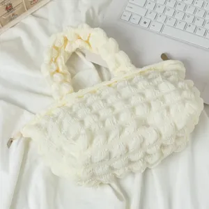 Vista detallada de un bolso de mano crema con textura de burbujas sobre fondo de tela
