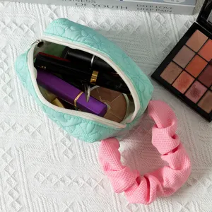 Close-up of mint green quilted makeup bag with pink ruffled handle filled with cosmetics