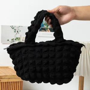 Detalle de bolso de mano negro con textura de burbujas y cierre superior de cremallera.